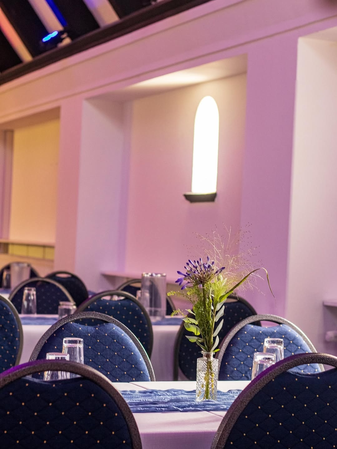 Gedeckte Tische mit blauen Stühlen und floraler Dekoration im Innenraum